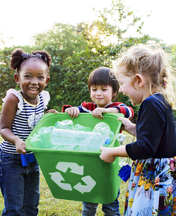 Three children proudly displaying a recycling receptacle full of plastic bottles